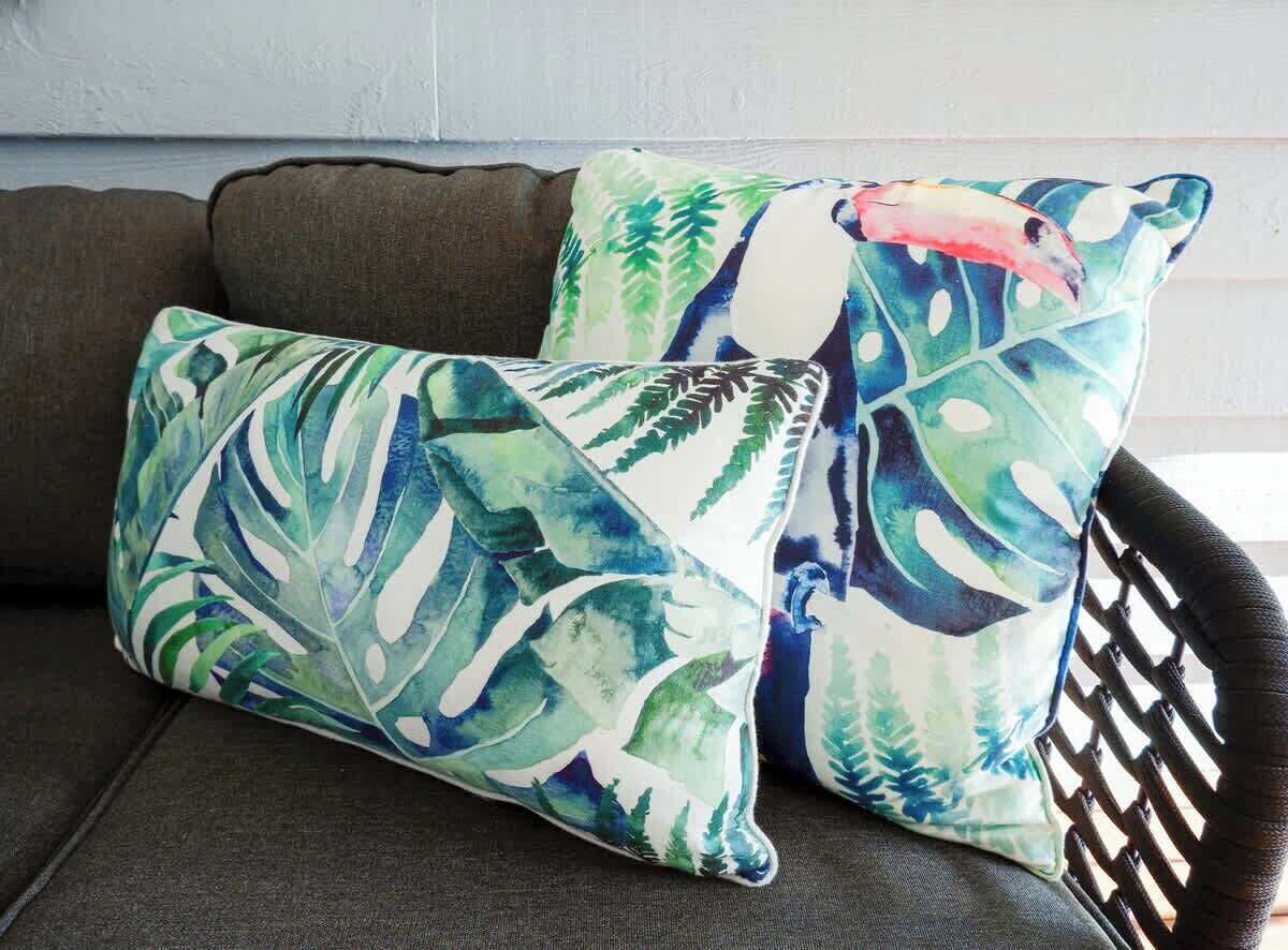 Two pillows with a tropical leaf pattern on a dark sofa.