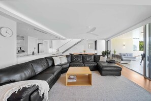 Ein modernes Wohnzimmer mit einem Ecksofa, einem Couchtisch aus Holz und einem großen Fenster mit Blick ins Freie.