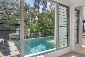 Una habitación con un amplio ventanal con vistas a una piscina y abundante vegetación.