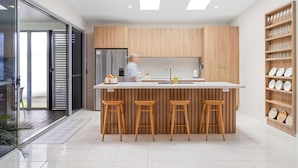 Una cocina moderna con una isla central, taburetes de madera y un ventanal que da a un balcón.