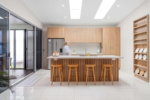 Una cocina moderna con una isla central, taburetes de madera y un ventanal que da a un balcón.