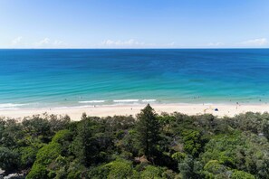 Una playa con aguas turquesas cristalinas, orilla de arena y exuberante follaje verde en primer plano.