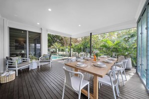 A spacious outdoor dining area with a wooden table set for six, surrounded by white chairs.