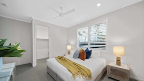 Un dormitorio con cama, mesitas de noche, ventilador de techo y ventana con persianas.