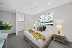 Un dormitorio con cama, mesitas de noche, ventilador de techo y ventana con persianas.