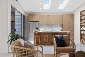 Una cocina moderna con armarios de madera, una isla central con taburetes y un comedor con mobiliario de mimbre.