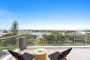 A balcony with two lounge chairs and a small table, overlooking a marina and cityscape.