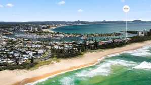 Vue aérienne d’une zone côtière comprenant un port de plaisance, une plage et des immeubles résidentiels.