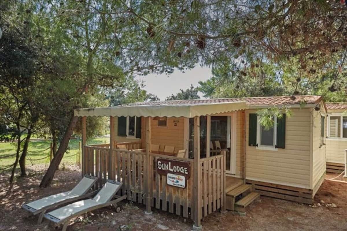 A small wooden cabin with a deck, two lounge chairs, and a sign reading "Sun Lodge."