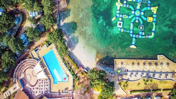 Vue aérienne d’un complexe hôtelier doté d’une piscine, d’une plage et d’une promenade en bord de mer.