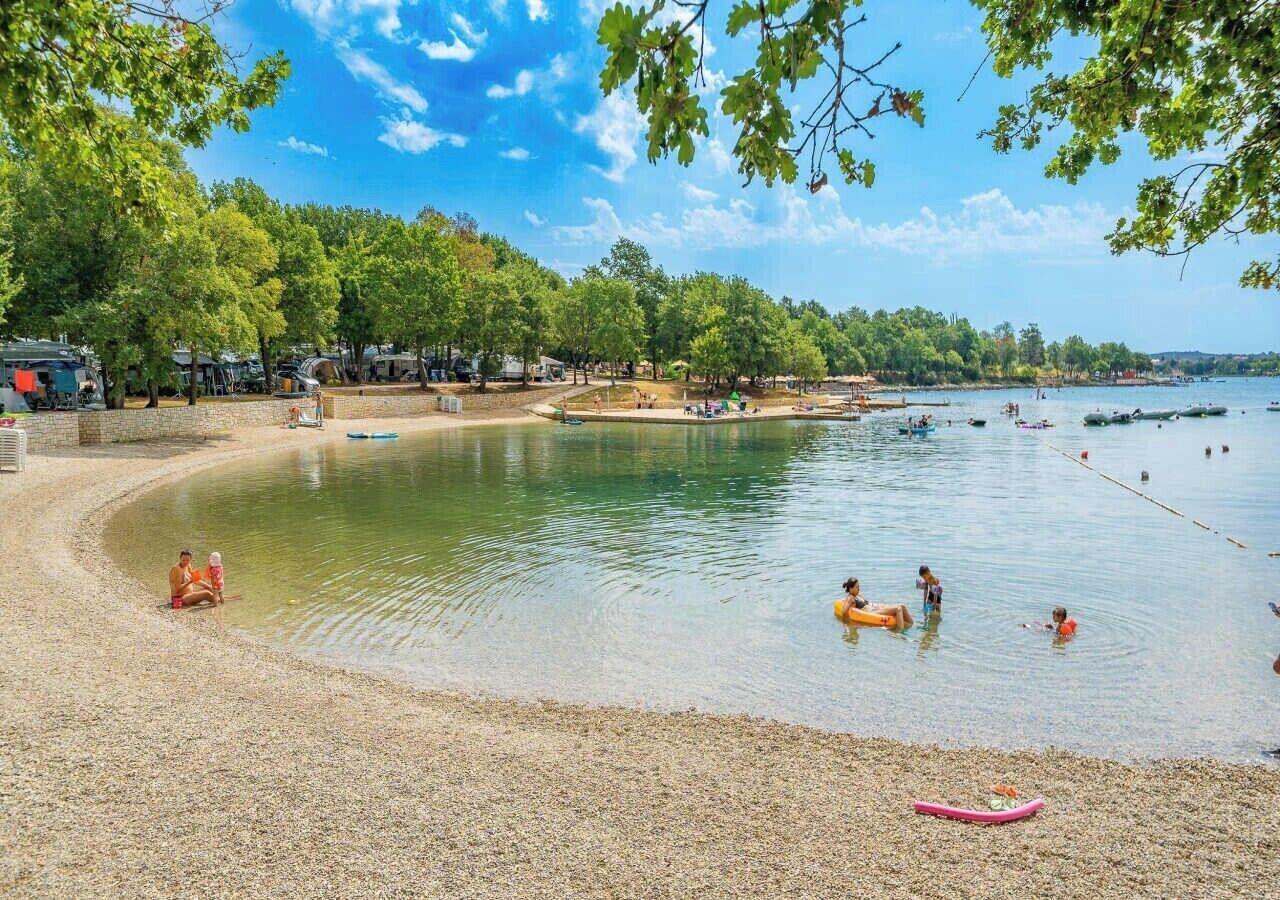 Une plage avec une eau cristalline, des gens qui se baignent et s’amusent, et des arbres en arrière-plan.