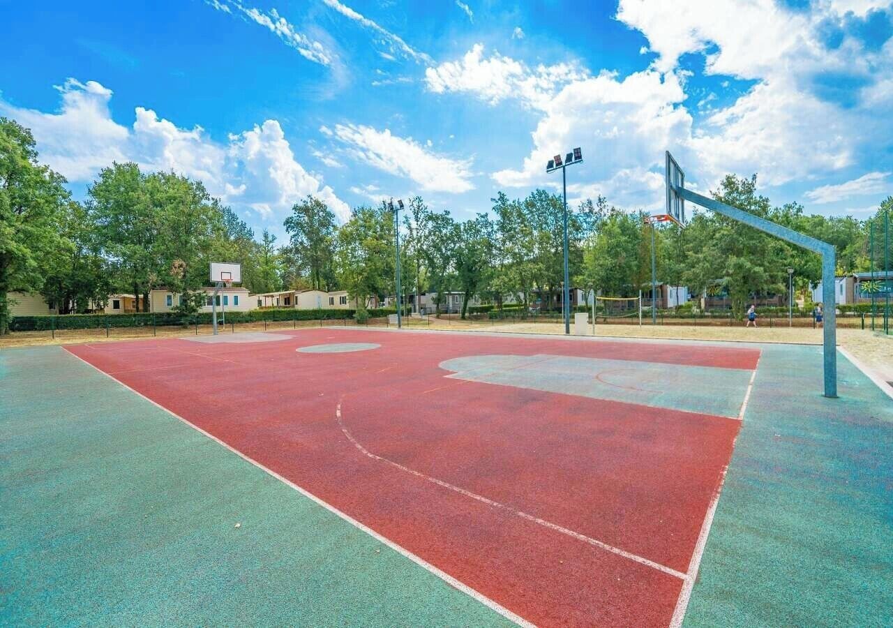 Un terrain de basket en plein air, doté d’une surface rouge et verte, entouré d’arbres et d’immeubles.