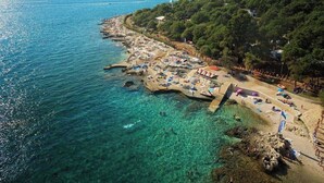 Une plage côtière aux eaux cristallines, bordée d’un littoral rocheux et entourée d’une zone boisée dense.