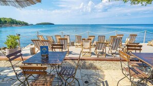 Un espace extérieur aménagé avec des chaises et des tables en bois, donnant sur une étendue d’eau.