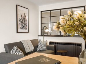 A modern living room with a sofa, a coffee table, a framed botanical print, a radiator, and a lamp. - Town Centre Studio Clifden (Clifden)