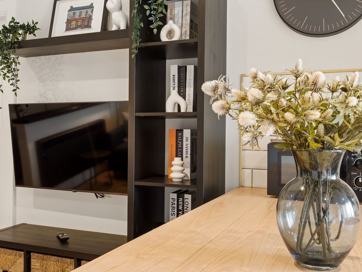 Een moderne woonkamer met een open haard, een boekenplank en een vaas met gedroogde bloemen op een houten tafel.