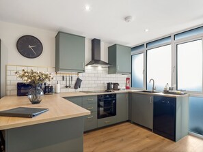 A modern kitchen with grey cabinets, a built-in oven, a microwave, and a large window providing natural light. - Town Centre Studio Clifden (Clifden)
