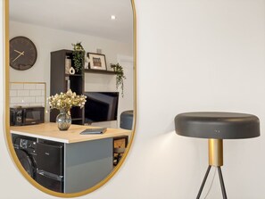 A modern kitchen with a round mirror, a dining area with a black chair, and a clock on the wall. - Town Centre Studio Clifden (Clifden)