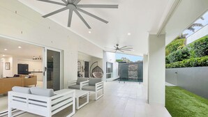Ein geräumiger Wohnbereich mit einem modernen Deckenventilator, einer Sitzgelegenheit mit weißer Möbel und Blick auf einen gepflegten Garten.