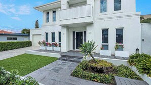 Ein modernes, zweistöckiges Haus mit Balkon, gepflegtem Rasen und einem Garten mit verschiedenen Pflanzen.