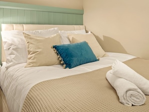 A neatly made bed with a beige headboard, white bedding, and a blue pillow with tassels.
