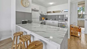 A modern kitchen with a large island, wooden stools, and a clock on the wall.