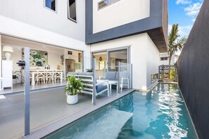 A modern house with a swimming pool, white furniture, and a dining area. - Luxury Living with Heated Pool in Birtinya (Mooloolaba Region)