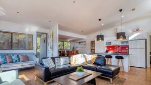 Uma sala de estar moderna com um sofá de couro preto, uma mesa de centro de madeira e uma área de cozinha com bancada vermelha e armários brancos.