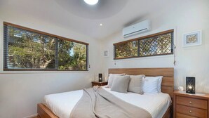 Quarto com cama de madeira, mesa de cabeceira, aparador e janela com vista para árvores.