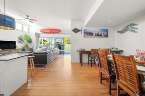 A modern kitchen with a dining area, wooden flooring, and a view to the outside.