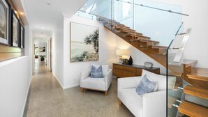 A modern interior with a staircase, a sofa, a chair, and a wall-mounted artwork. - Golden Beach Luxury for Families (Caloundra Region)