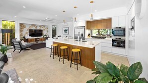 A modern kitchen with a central island, bar stools, and a large TV. - Golden Beach Luxury for Families (Caloundra Region)