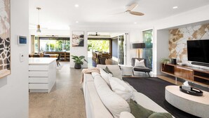 A modern living room with a sofa, TV, and dining area. - Golden Beach Luxury for Families (Caloundra Region)
