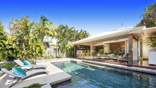A modern pool area with lounge chairs, a glass-enclosed patio, and tropical vegetation. - Golden Beach Luxury for Families (Caloundra Region)
