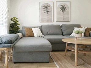 A grey sectional sofa with a round wooden coffee table, a small potted plant, and two framed artworks on the wall.