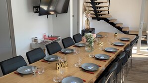 A modern dining area with a long wooden table set for a meal, black chairs, and a TV mounted on the wall. - Le Gîte du Plessis Montanel - 12 people, 25 minutes from Mont Saint-Michel (Saint-James)