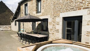 A stone building with a patio area featuring a table and chairs, a hot tub, and an umbrella. - Le Gîte du Plessis Montanel - 12 people, 25 minutes from Mont Saint-Michel (Saint-James)