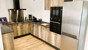 A modern kitchen with wooden cabinets, stainless steel appliances, and a built-in oven. - Le Gîte du Plessis Montanel - 12 people, 25 minutes from Mont Saint-Michel (Saint-James)