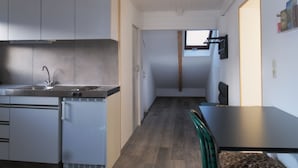 Cocina compacta con electrodomésticos modernos, comedor con mesa y sillas, y vista de la habitación contigua a través de una puerta.