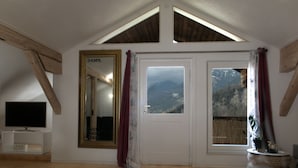 Una habitación con techo inclinado, un espejo grande, un televisor y vistas a montañas a través de una ventana.