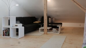 Un dormitorio estilo loft moderno con techo inclinado, un sofá negro, mesitas de noche blancas y estructura de vigas de madera.
