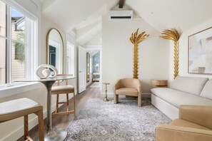 A modern living room with a sofa, a coffee table, and a chair. There is a large mirror on the wall, a tall decorative plant, and a framed picture. - The Pink Palm | Private Pool | Bach Trip Paradise (Charleston)