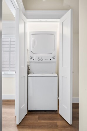A compact, white laundry room with a built-in washer and dryer, wooden flooring, and a white door.
