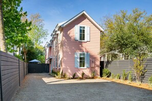 A pink two-story house with a driveway leading to a black gate.