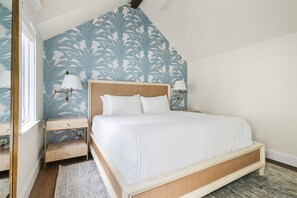 A bedroom with a bed, two bedside tables, and a wall with a leaf pattern. - The Pink Palm | Private Pool | Bach Trip Paradise (Charleston)