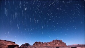 A star trail over a desert landscape with several black tents arranged in rows. - Wadi Rum Heritage (Wadi Rum)