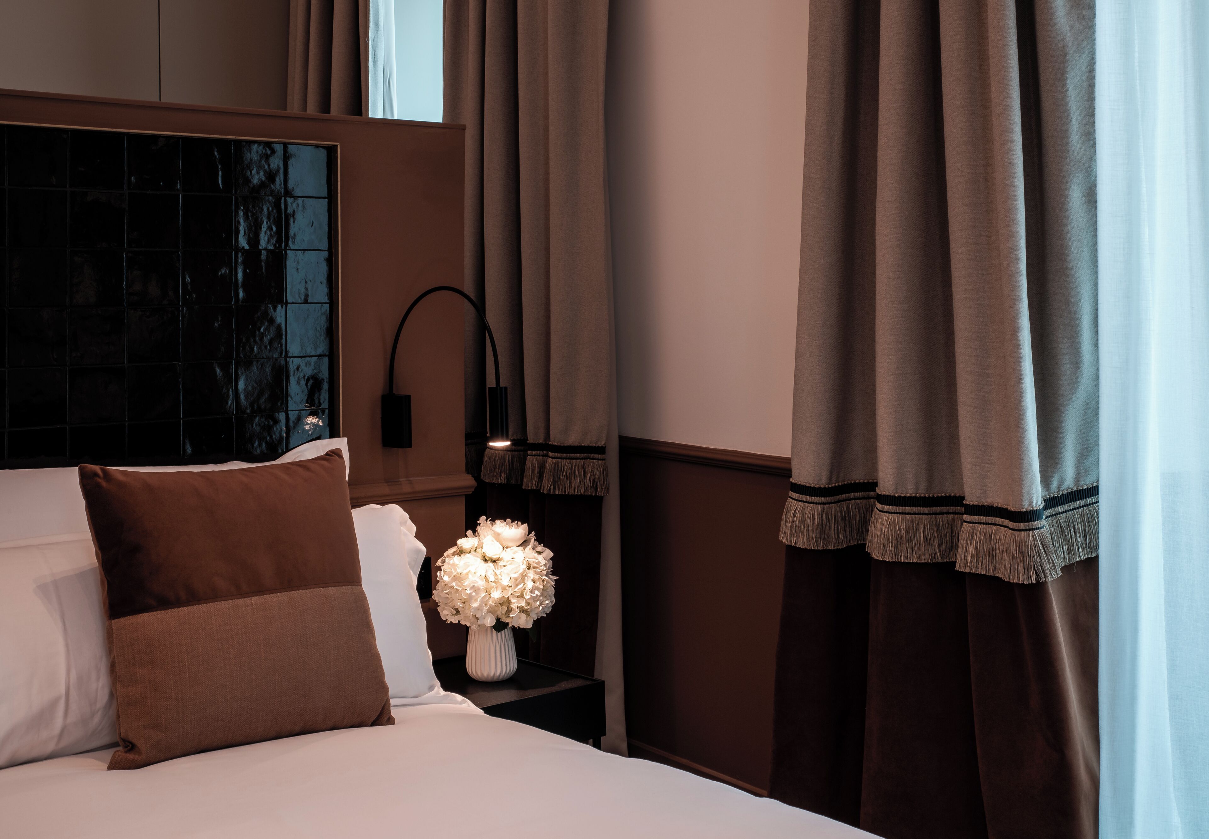 Une chambre d’hôtel avec un lit, une table de chevet ornée d’un vase de fleurs et des rideaux.