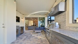 Eine moderne Küche mit integriertem Grill, einem Essbereich mit einer Couch und einem Boden aus Steinplatten.