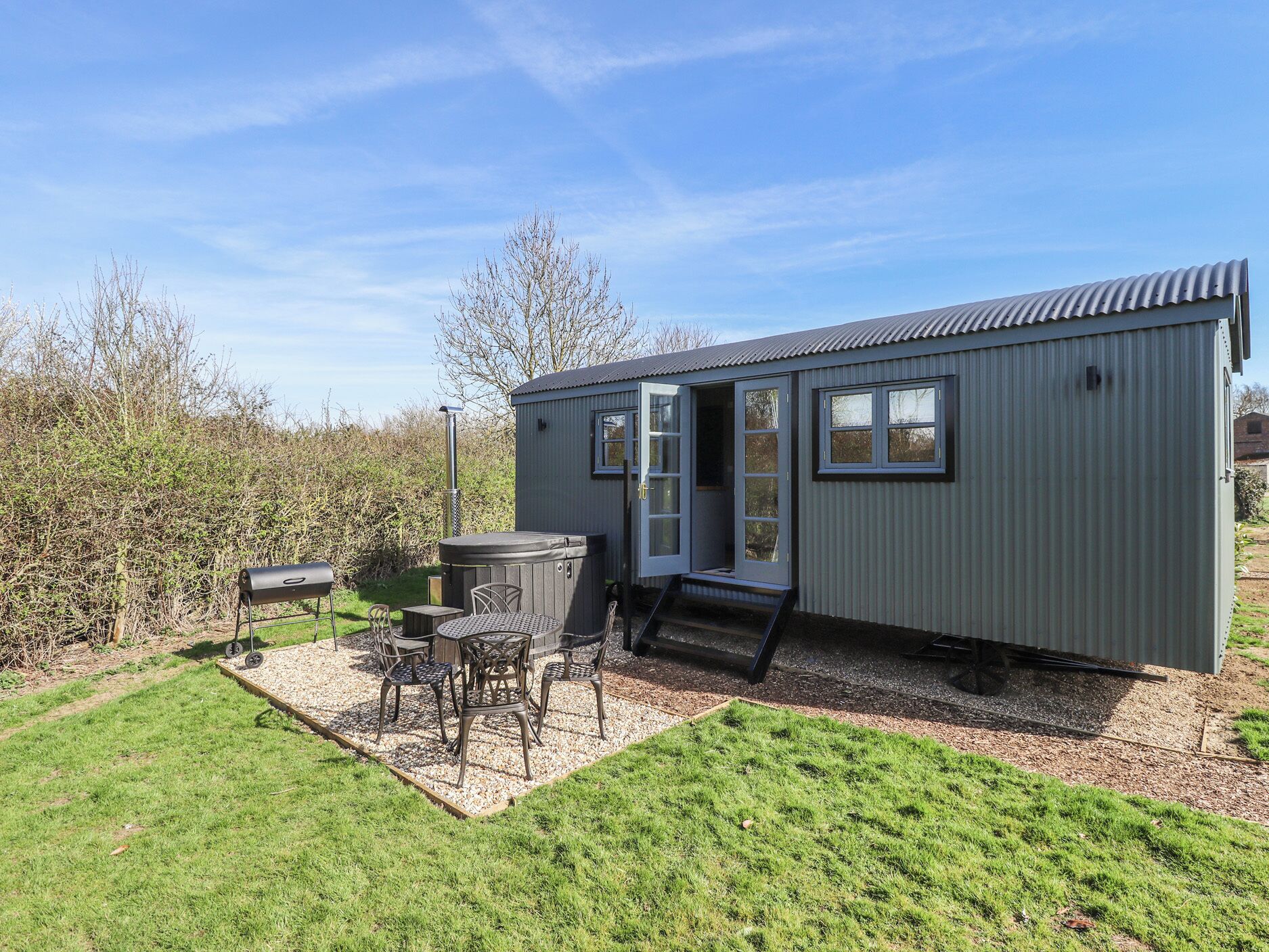 A compact, single-story building with a flat roof, a small patio area with a hot tub, and a grill.