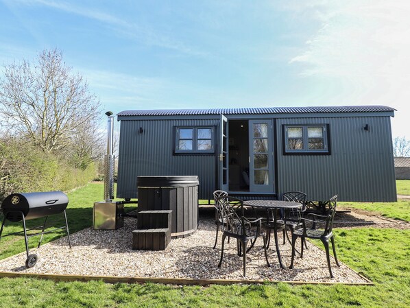 A compact, single-story metal building with a door and windows, a barbecue grill, and a table with chairs in front. - Dandelion (Grimsby)